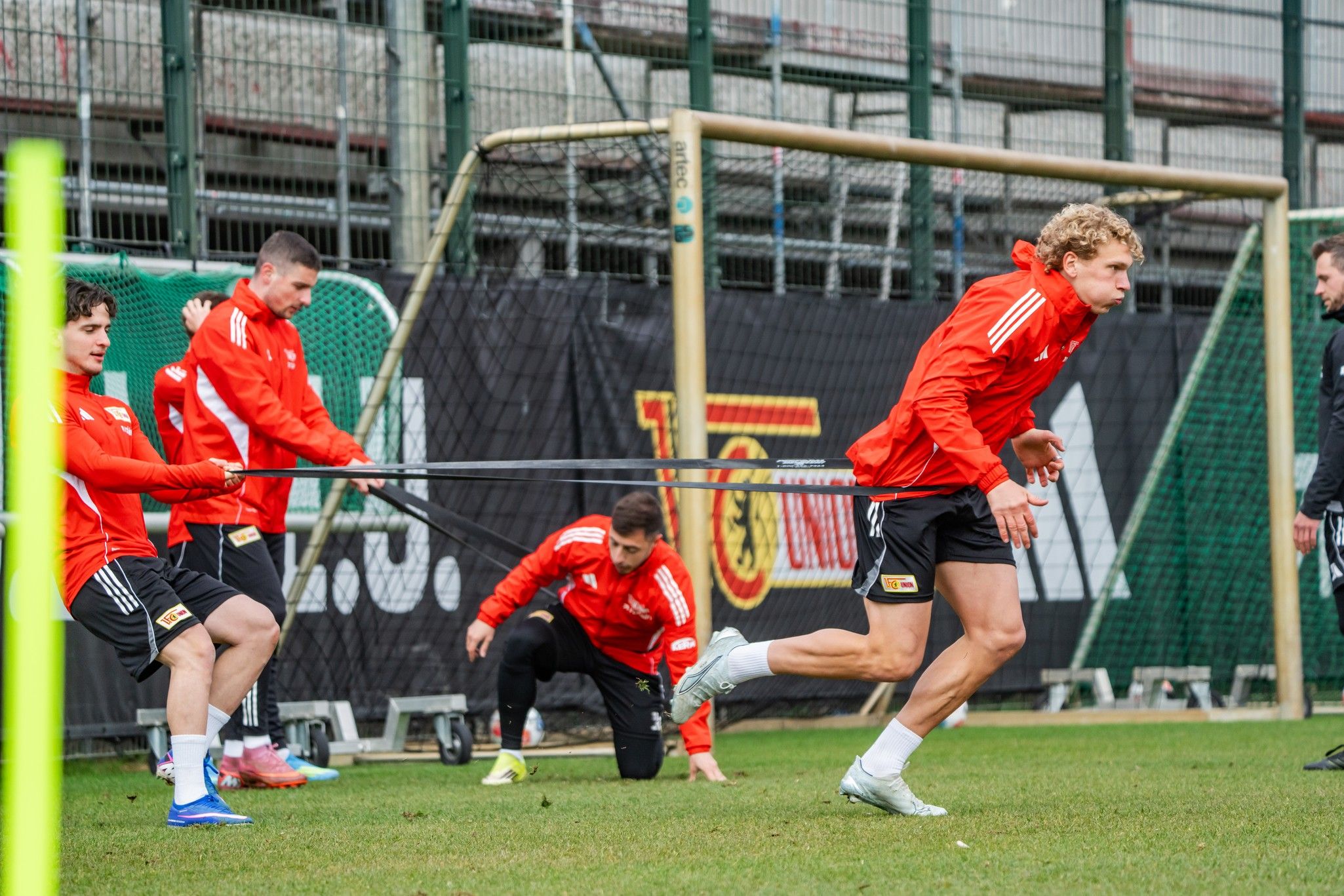 Spieler in rot-weißer Trainingskleidung machen ein Fitnesswochenende, während einige mit einem Widerstandsband trainieren.