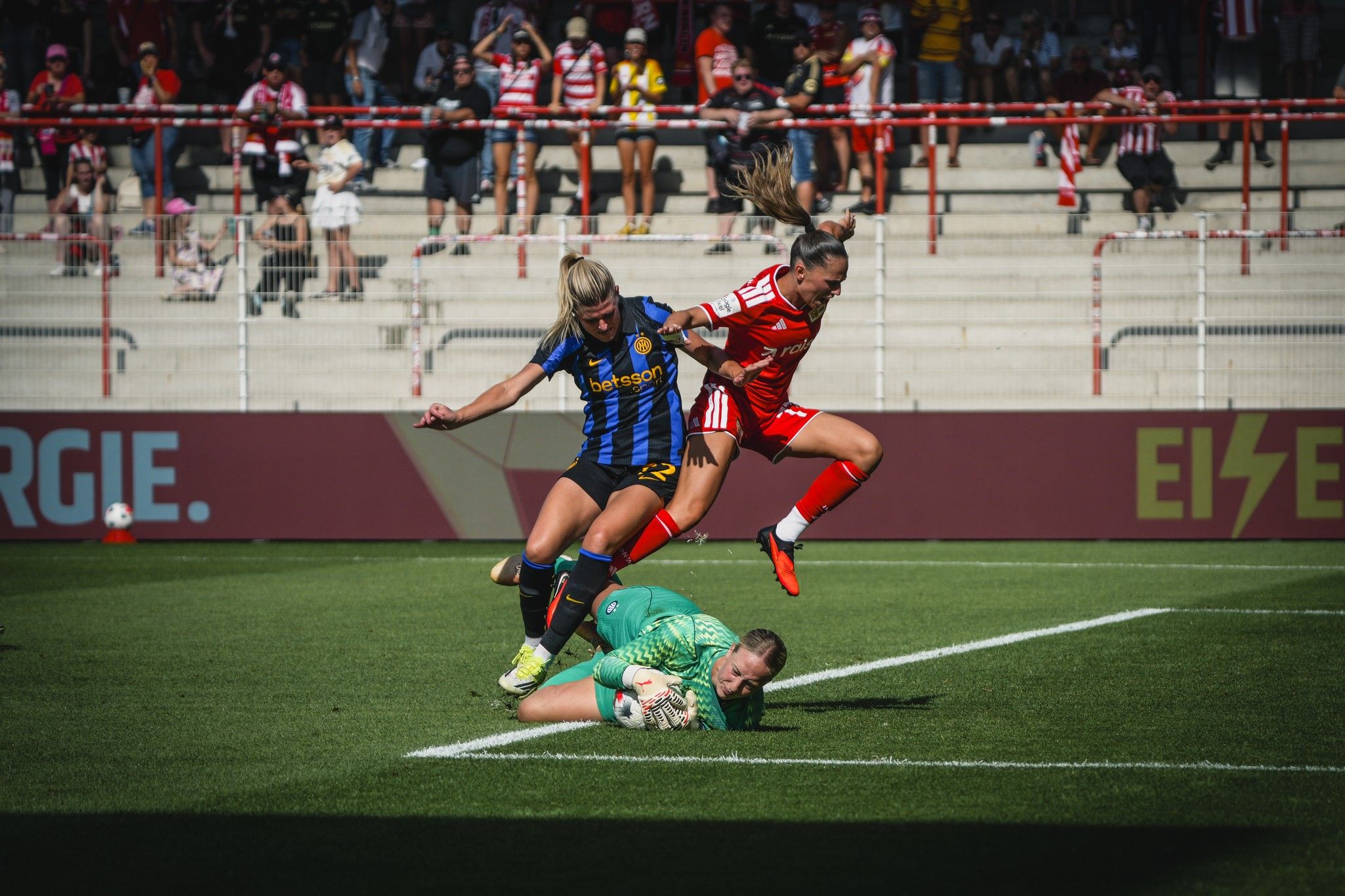 Eine Torhüterin fängt den Ball, während zwei Spielerinnen in einem spannenden Moment des Spiels um den Ball kämpfen.