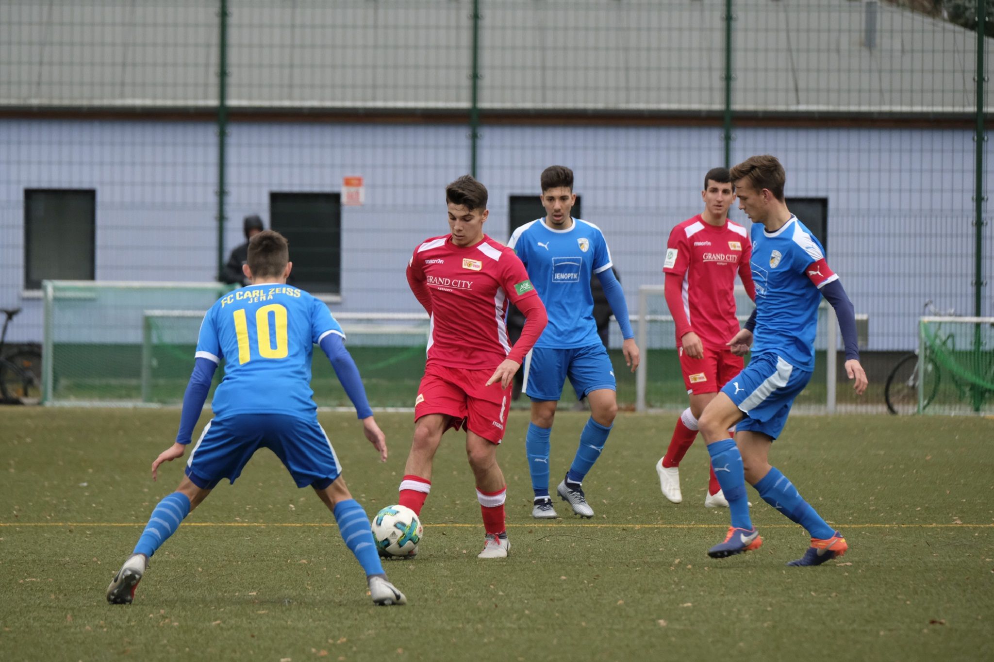 Zwei Gruppen von Fußballspielern in roten und blauen Trikots stehen auf einem Rasenplatz und kämpfen um den Ball.