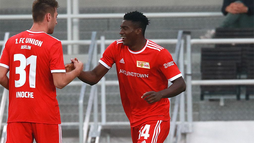 Zwei Fußballspieler des 1. FC Union Berlin in roten Trikots feiern einen Erfolg auf dem Spielfeld.