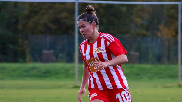 Junge Fußballspielerin in rotem Trikot mit weißen Streifen läuft über das Feld.