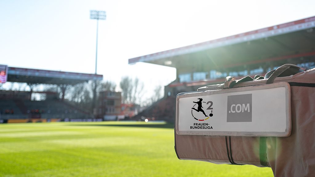 Ein Fußballfeld im Stadion mit einer Tasche, auf der "FRAUEN-BUNDESLIGA" und ".COM" steht, im Hintergrund steht das Stadion.
