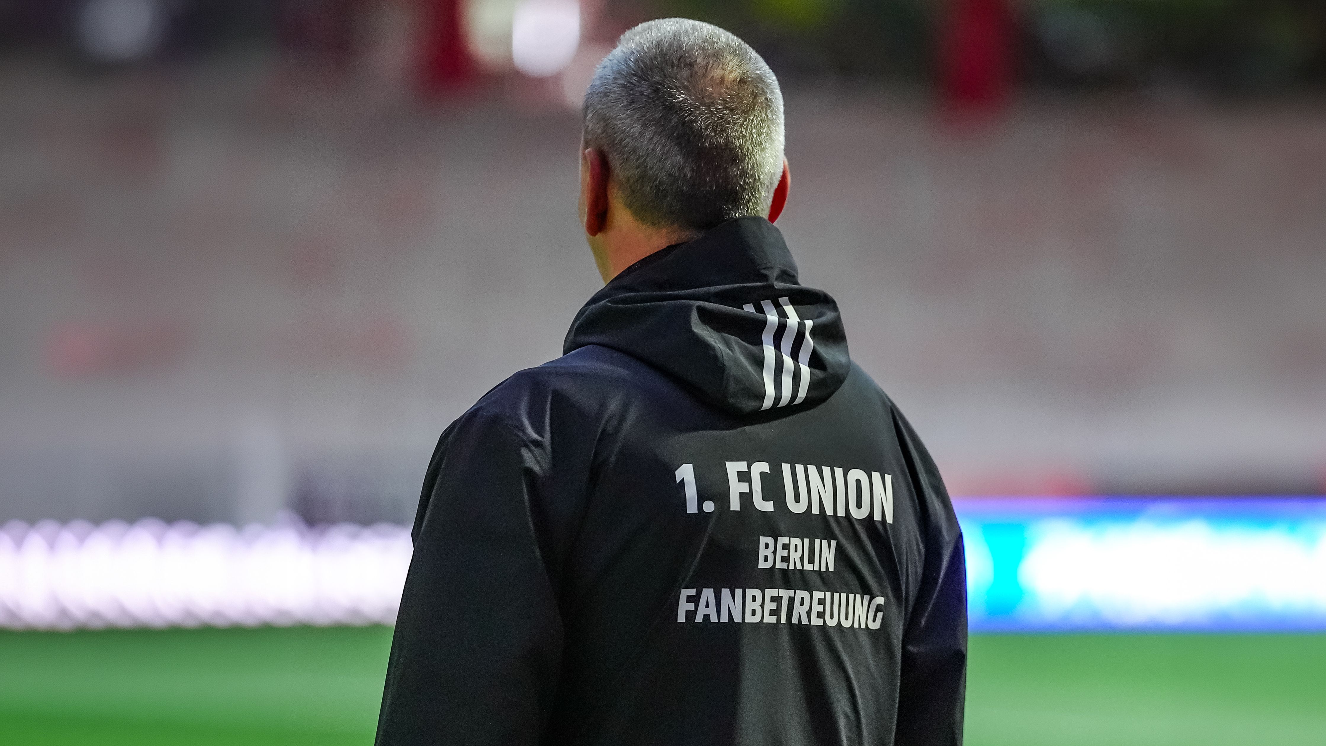 Mann mit grauen Haaren von hinten, trägt eine schwarze Jacke mit dem Aufdruck "1. FC UNION BERLIN FANBETREUUNG".