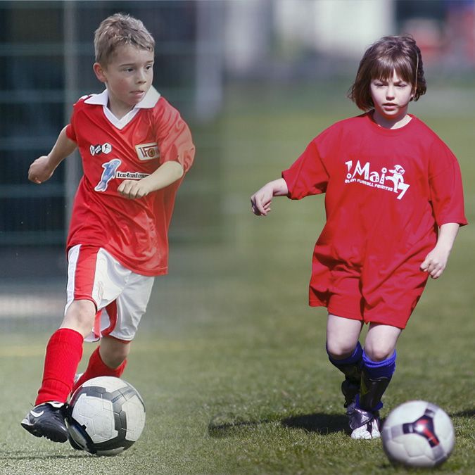 Zwei Kinder spielen Fußball, eines in rotem Shirt und eines in rotem T-Shirt, beide mit einem Fußball auf einem grünen Feld.