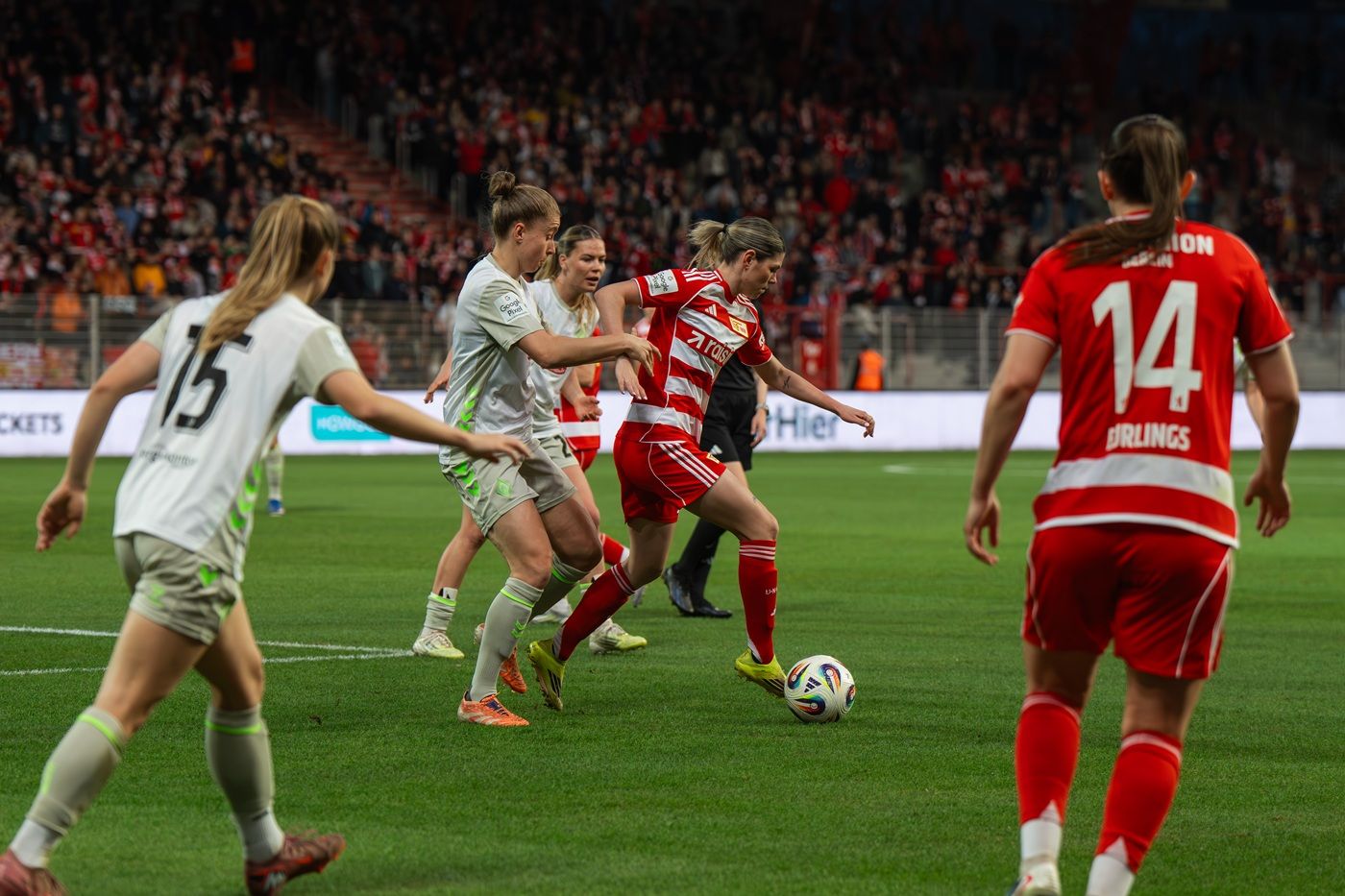 Zwei Frauenfußballmannschaften im Wettbewerb auf dem Spielfeld während eines Spiels, mit Spielern in roten und grauen Trikots.