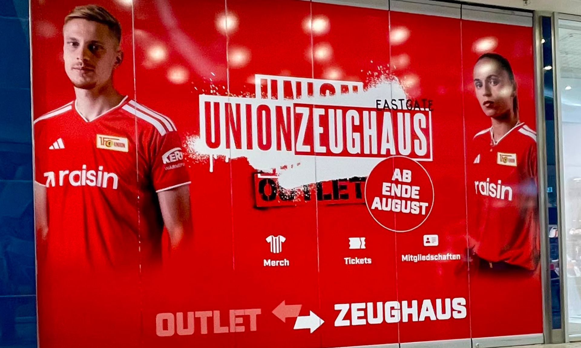 Werbung für das Union-Zeughause mit einem roten Hintergrund, zwei Spielern und Hinweisen auf Merchandise und Mitgliedschaften.