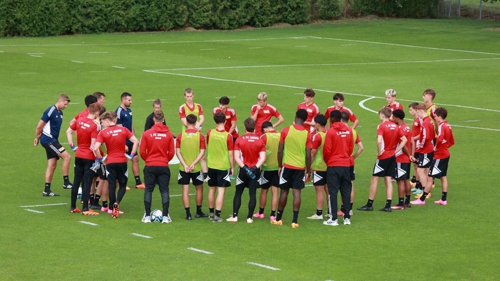 Eine Gruppe von Fußballspielern in roten Trikots versammelt sich zu einer Besprechung auf einem Sportplatz.