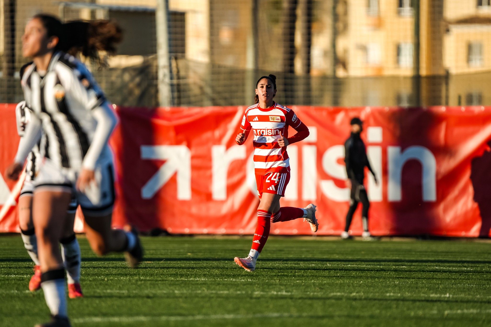 Eine Fußballspielerin in roter und weißer Uniform sprintet über das Spielfeld, während andere Spielerinnen im Hintergrund laufen.