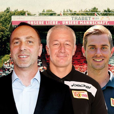 Drei Männer stehen vor einem Stadion mit einer großen Banner, die den Slogan „Unsere Liebe. Unsere Mannschaft.” zeigt.