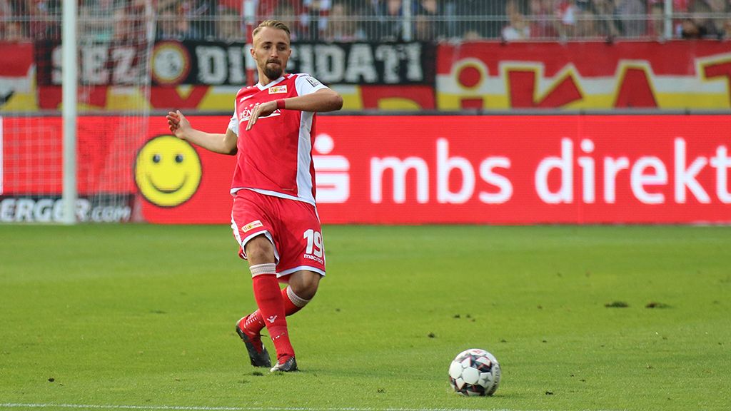 A football player in a red jersey is making a pass while spectators cheer in the background.