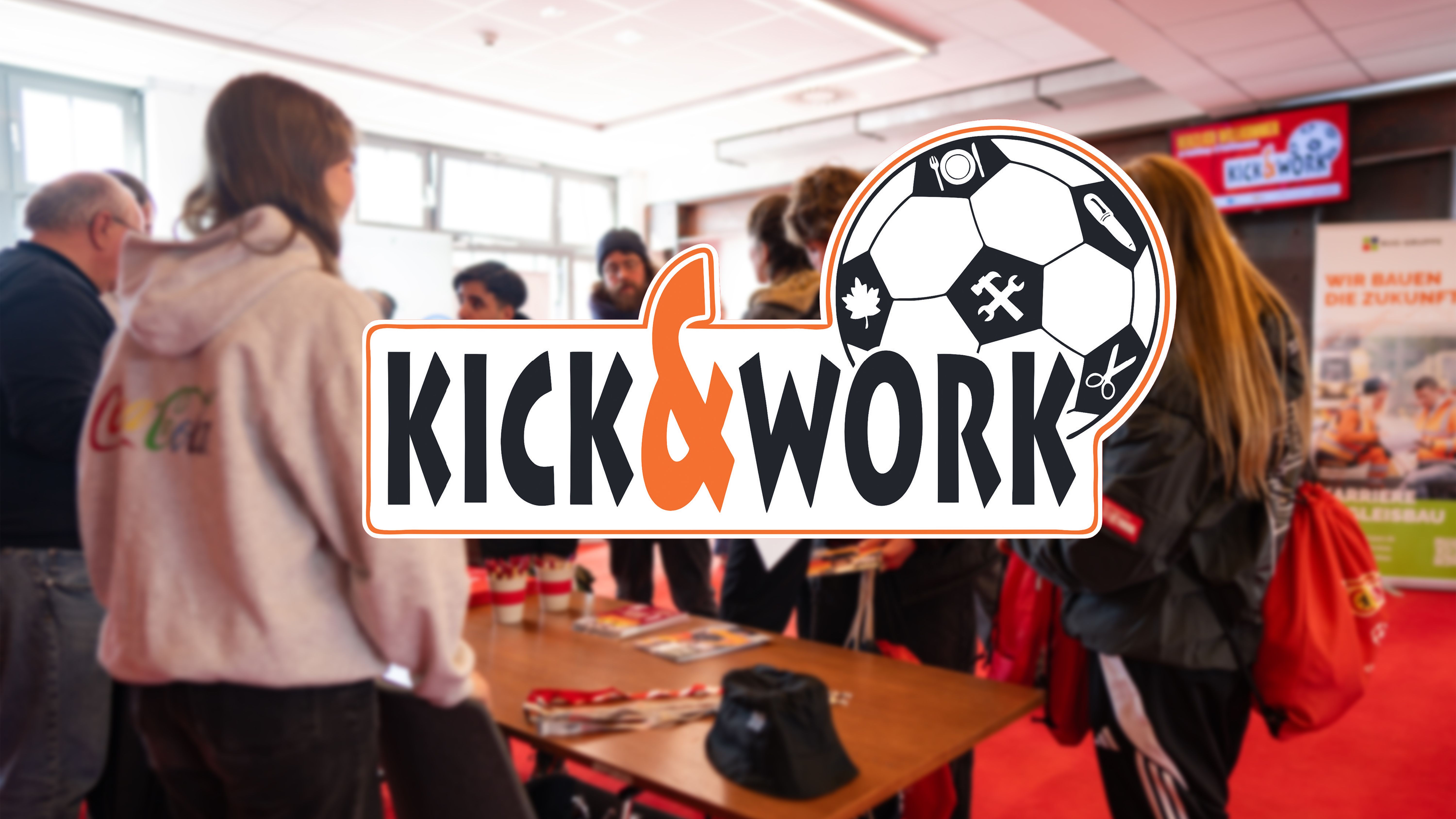 Menschen stehen an einem Tisch bei einer Veranstaltung mit dem Logo "KICK & WORK" im Vordergrund.