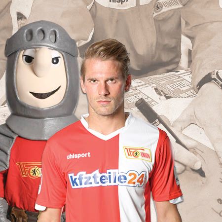 Ein Fußballspieler in rot-weißer Teamkleidung steht neben einem maskottchenhaften Ritter. Im Hintergrund sind unscharfe alte Fotos zu sehen.
