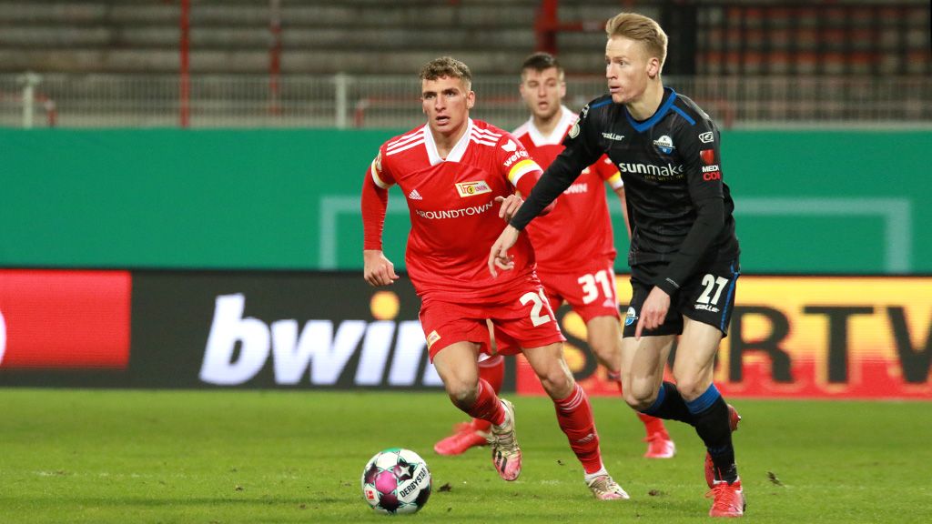 Zwei Fußballspieler im Wettlauf um den Ball während eines Spiels, einer in rotem und der andere in schwarzem Trikot.