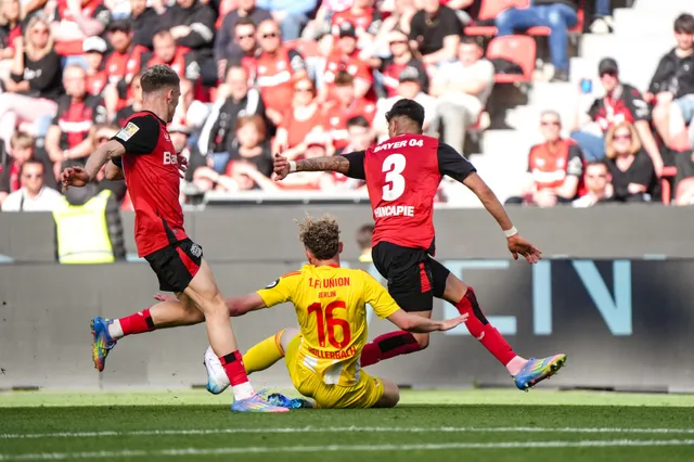 Zwei Fußballspieler in roten Trikots, die einen dritt Spieler in gelbem Trikot angreifen, während Zuschauer im Hintergrund jubeln.