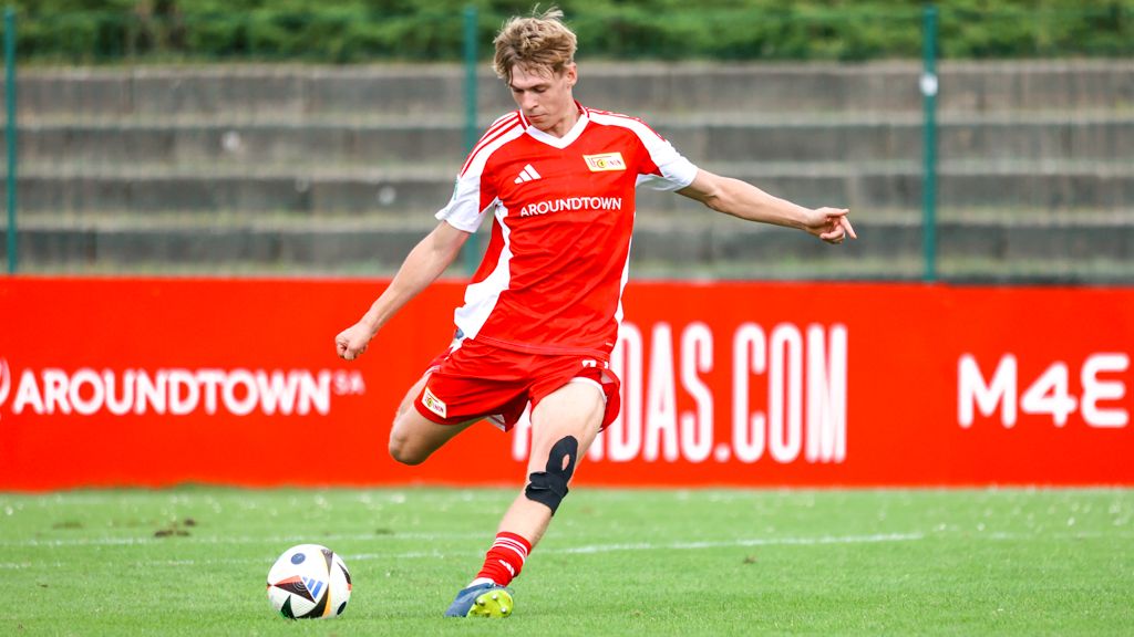 Ein junger Fußballspieler in rotem Trikot läuft über ein Trainingsfeld und spielt mit einem Ball.
