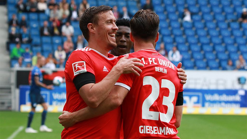 Zwei Spieler des 1. FC Union Berlin feiern einen Torerfolg im Stadion, während ein weiterer Spieler im Hintergrund steht.