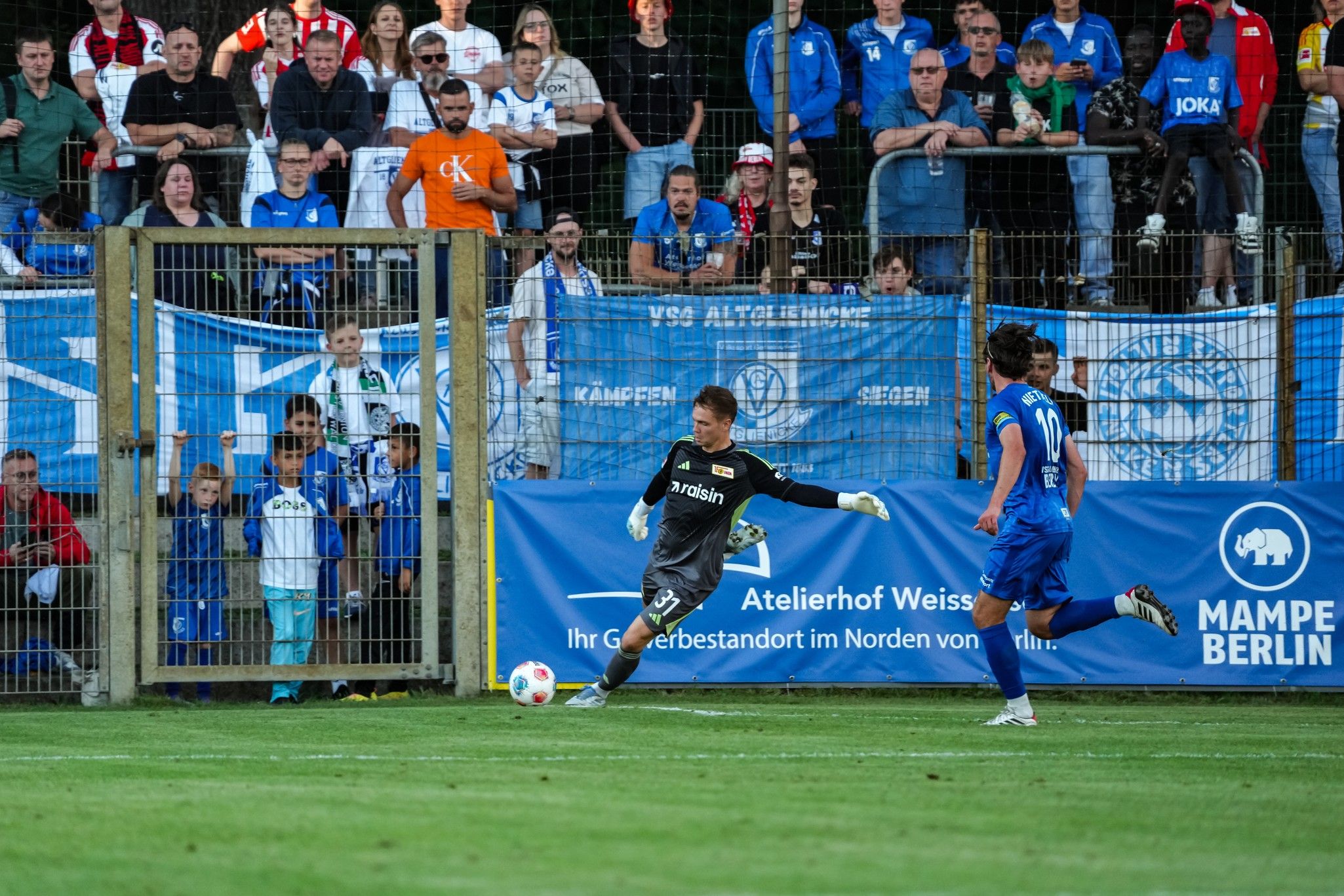 Ein Torwart tritt den Ball während eines Fußballspiels, Zuschauer jubeln im Hintergrund.