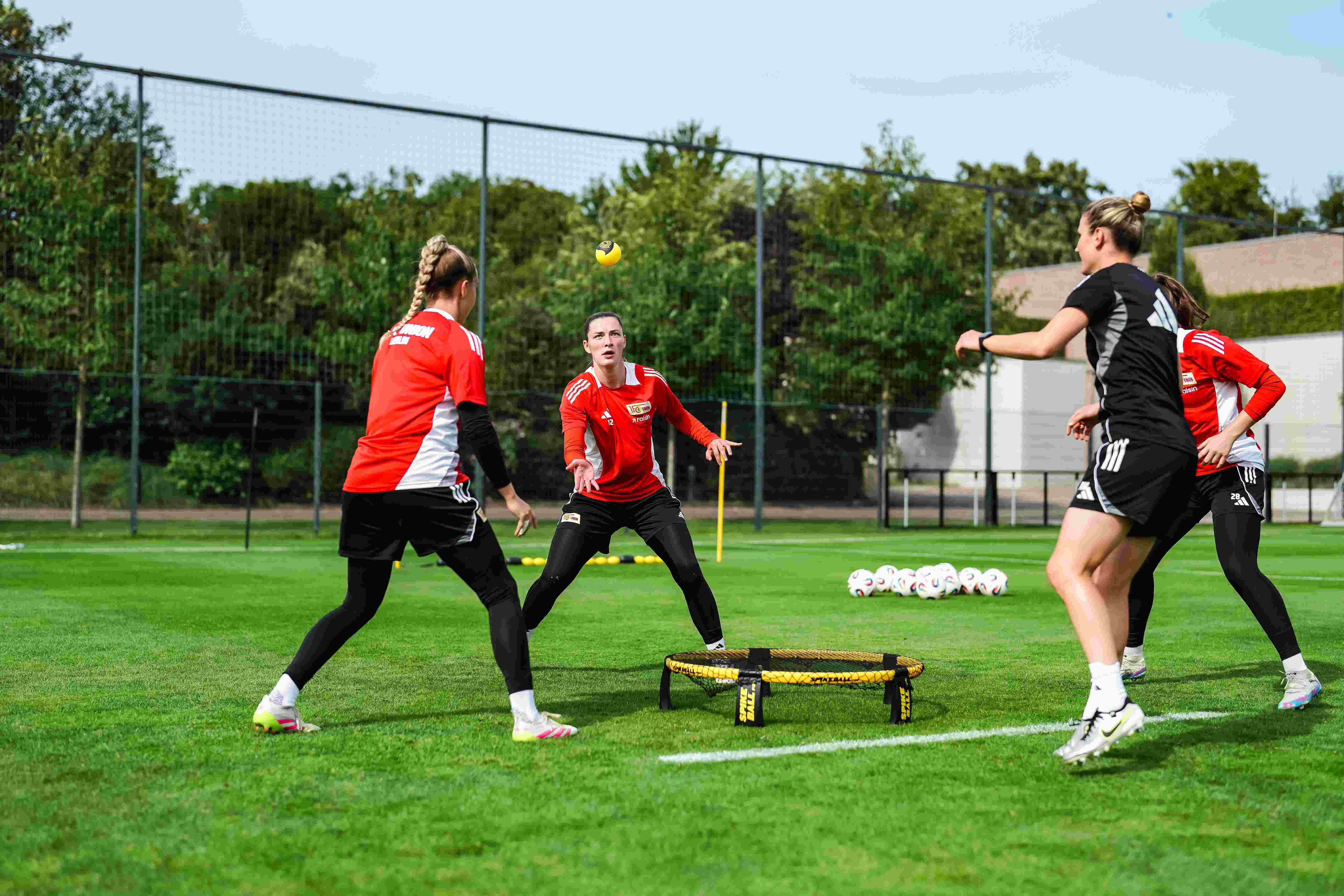 Four women in training on a football field use a coaching tool to practice ball control.