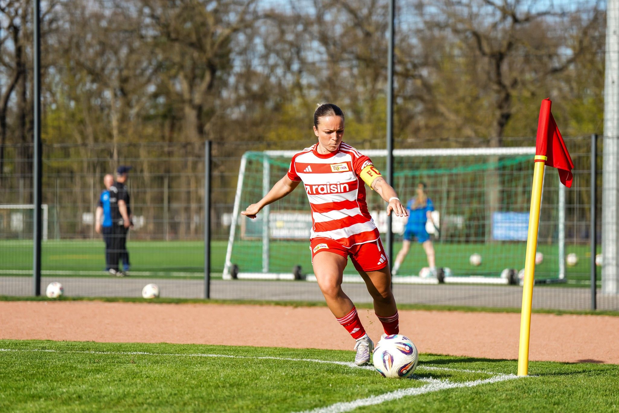 Spielerin in rotem Trikot mit weißen Streifen führt einen Eckstoß auf einem Fußballplatz aus.
