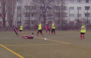 Zwei Gruppen von Spielern trainieren auf einem Fußballfeld, einer fällt zu Boden, während ein Ball in der Nähe rollt.