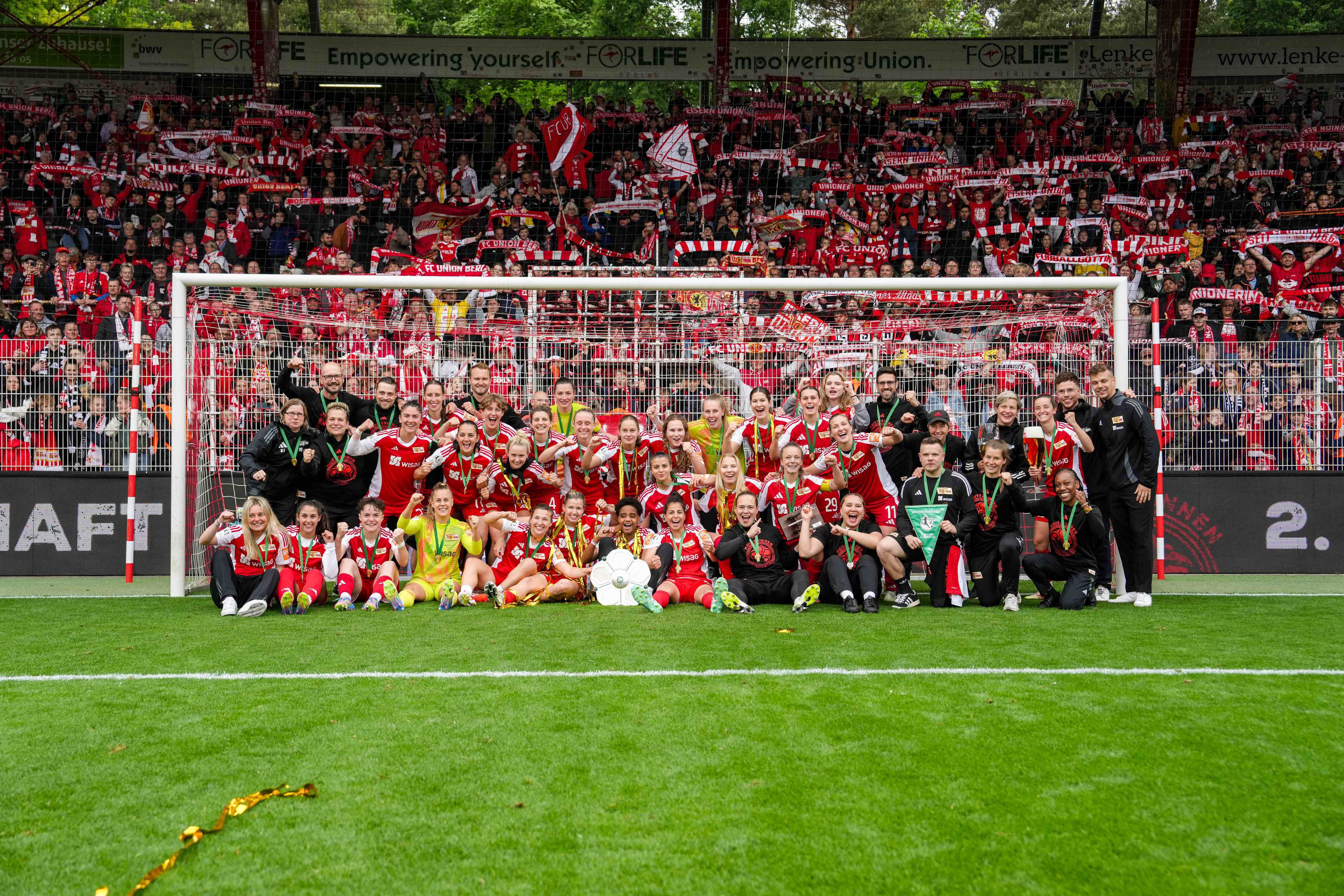 Un equipo de fútbol celebrando con seguidores, posando frente al arco y festejando una victoria o un título.