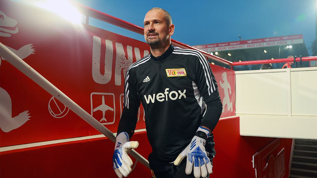 Torwart in Fußballkleidung, der eine Treppe hinuntergeht, mit Handschuhen und konzentriertem Blick.