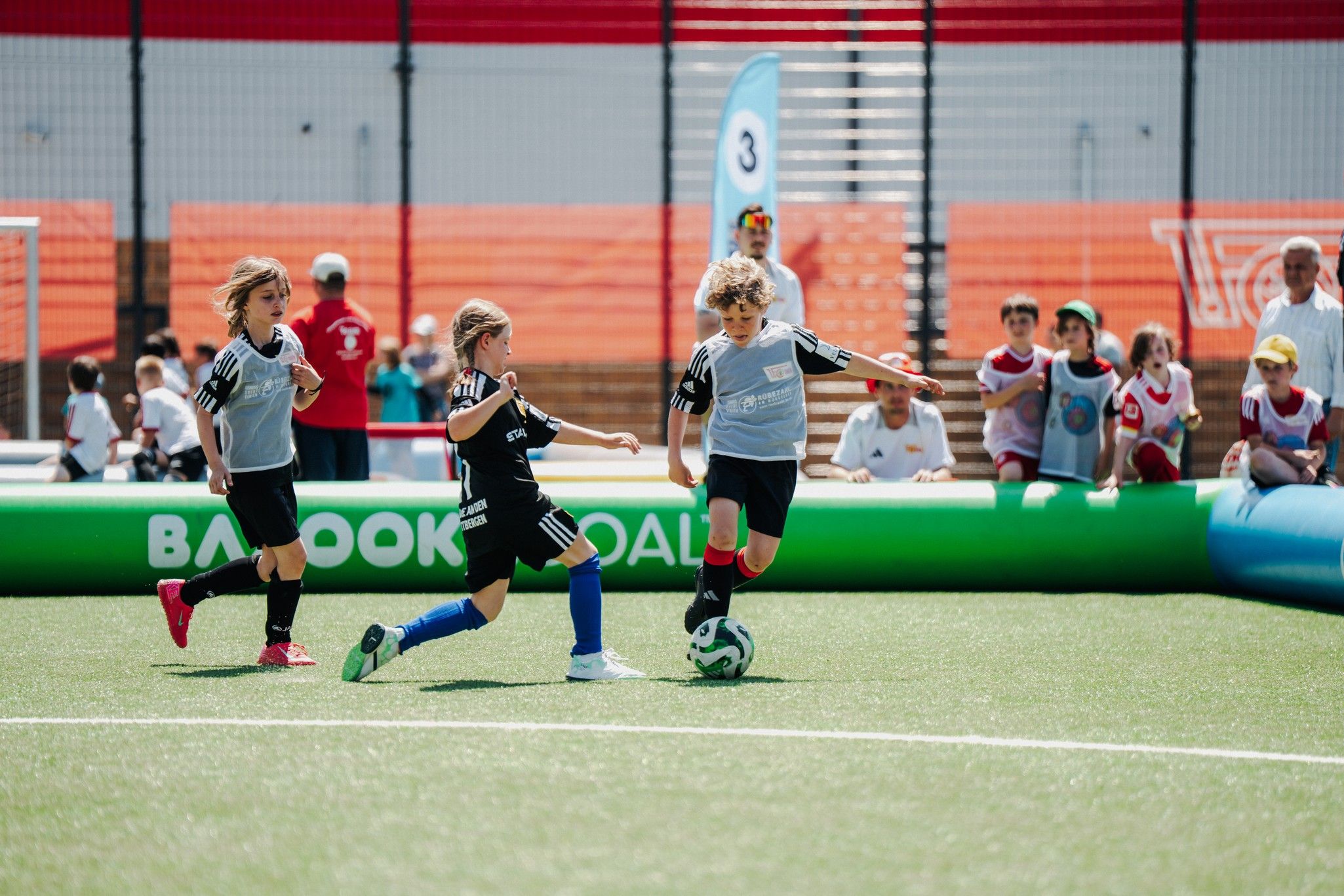Zwei Kinder im Fußballspiel dribbeln den Ball, während ein drittes Kind in blauer Trikots rechts daneben steht.