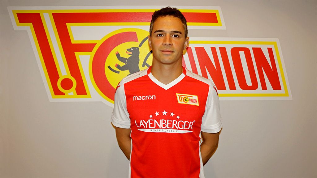 Ein junger Mann in einem Fußballtrikot des 1. FC Union steht vor einer Wand mit dem Vereinslogo.