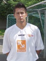 Ein junger Mann im weißen Fußballtrikot steht vor einem Fußballtor.