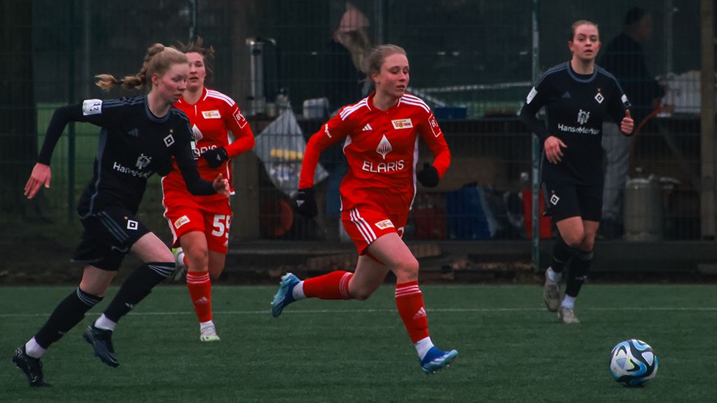 Zwei Frauenfußballspielerinnen in Aktion auf dem Spielfeld, eine in rotem Trikot, die andere in schwarzem Trikot.