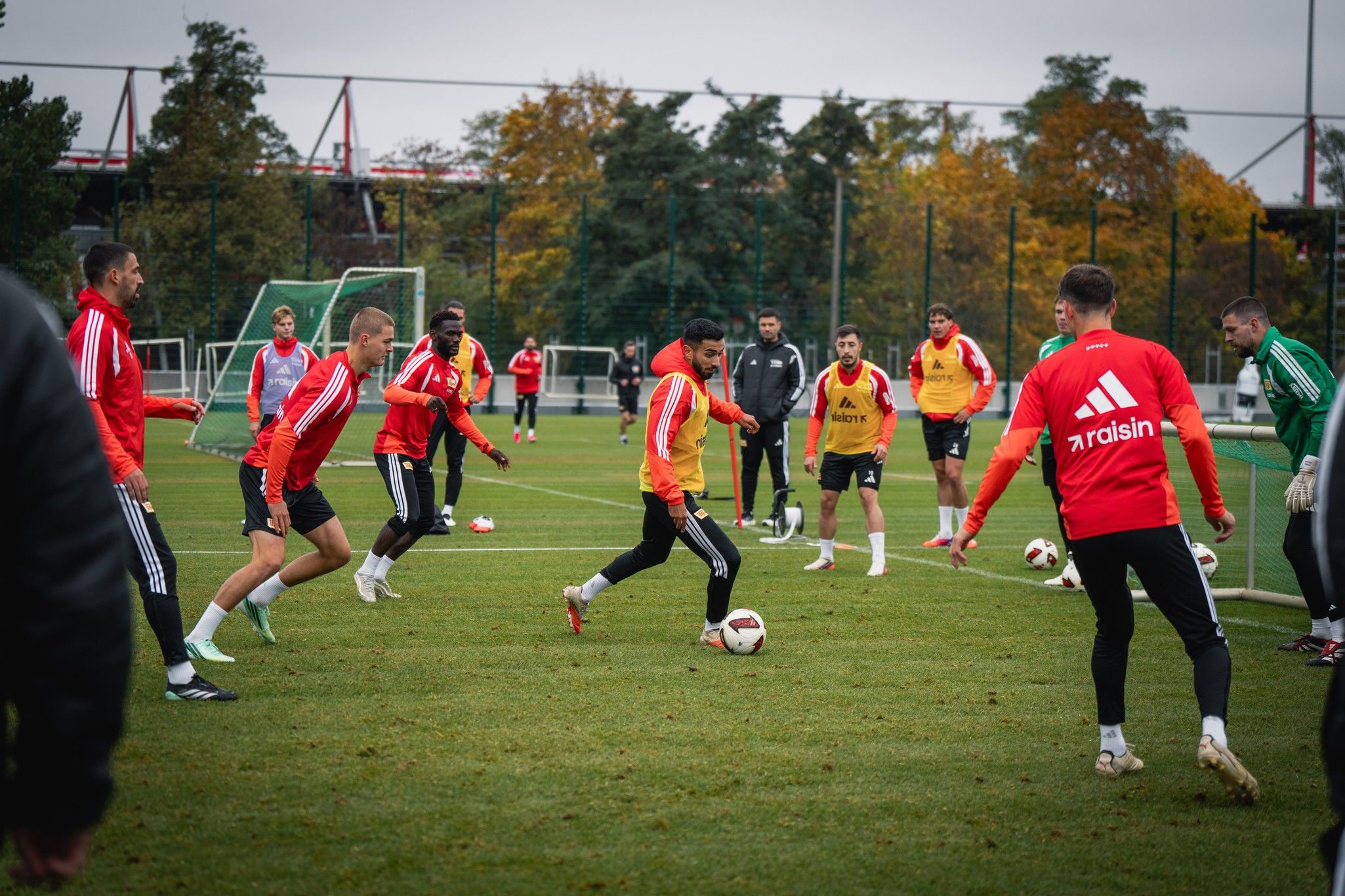 Fußballmannschaft trainiert auf einem Rasenplatz, Spieler in roten Trikots dribbeln und passen den Ball.