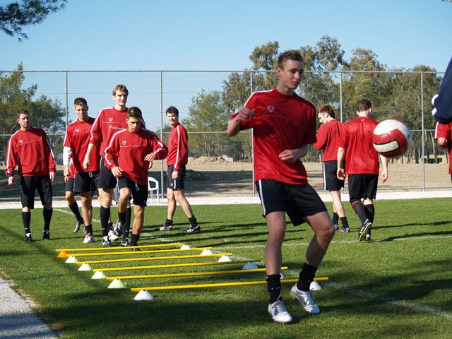 Eine Gruppe von Fußballspielern in roten Trikots trainiert auf einem Platz mit Hütchen und Übungen auf dem Rasen.