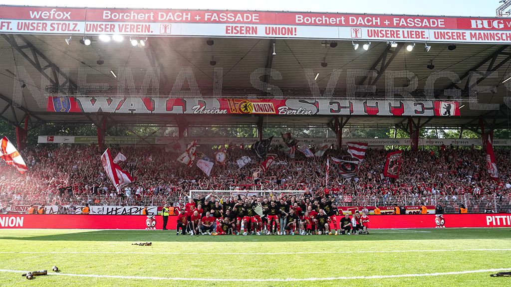 Eine große Menschenmenge mit Flaggen und Bannern im Stadion, jubelnd und feiernd, während sie eine Sportmannschaft unterstützen.
