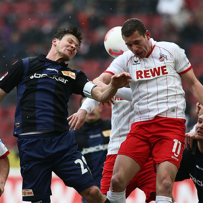 Spielszene im Fußball mit zwei Spielern, die um den Ball kämpfen, während weitere Spieler im Hintergrund zu sehen sind.