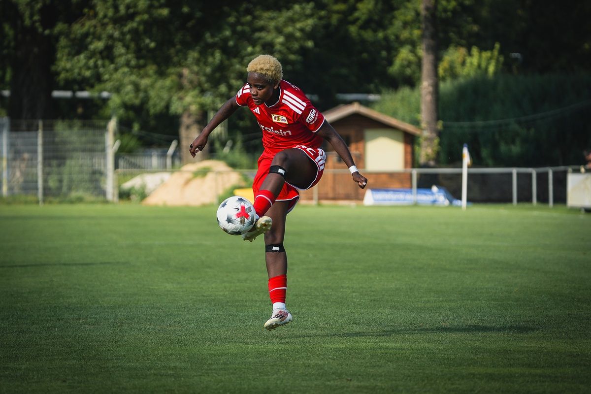 Ein Fußballspieler in rotem Trikot jongliert einen Ball auf einem Rasenfeld.