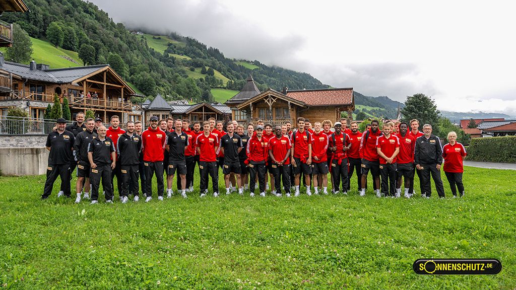 Group photo of a sports team in uniform clothing, taken outdoors in front of a picturesque mountain landscape.