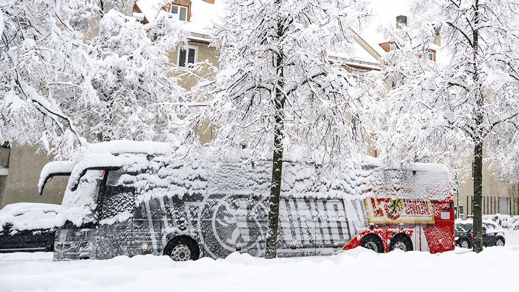 Ein Lkw steht unter schneebedeckten Bäumen in einer verschneiten Straße, die von frostigem Wetter geprägt ist.