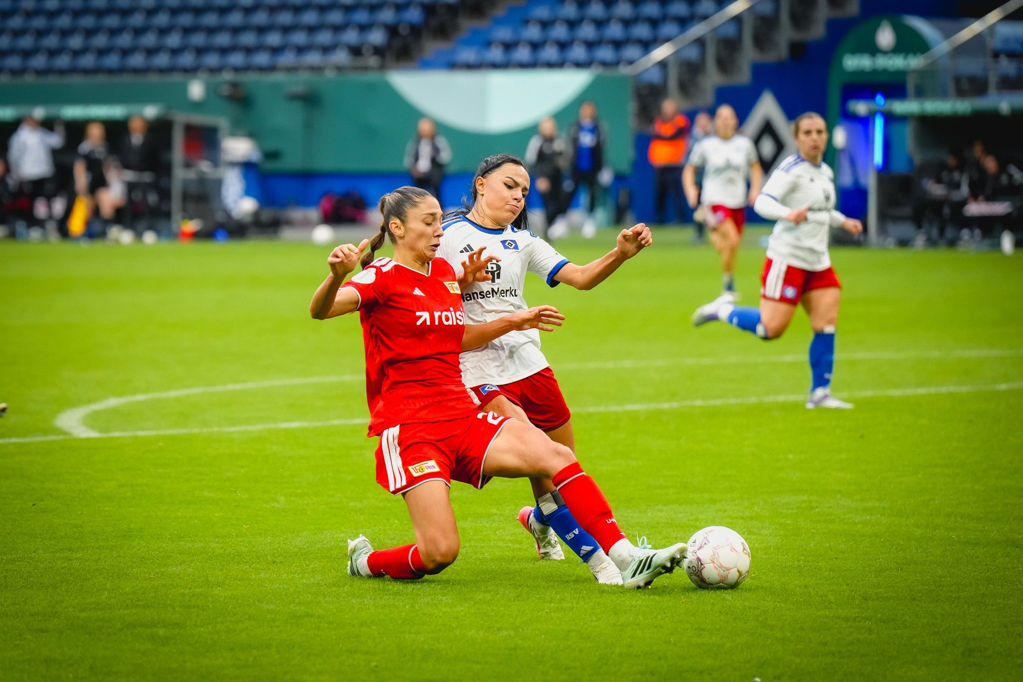 Zwei Fußballspielerinnen kämpfen um den Ball auf einem grünen Spielfeld während eines Spiels.