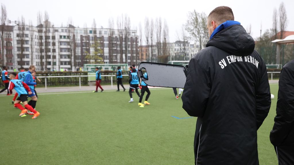 Ein Trainer beobachtet eine Jugendfußballmannschaft beim Training auf einem Rasenplatz.