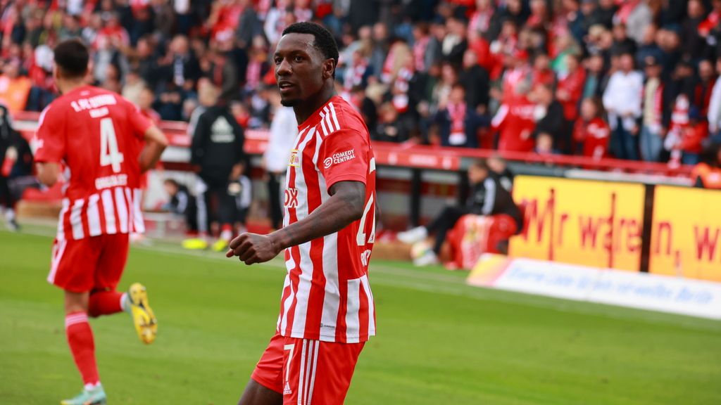 Ein Fußballspieler in roter und weißer Uniform jubelt vor einer jubelnden Menge im Stadion.