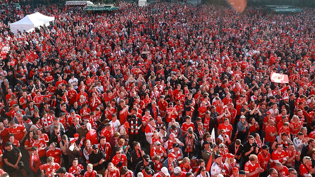 A large crowd is wearing red clothing and cheering, likely at a sports event or celebration.