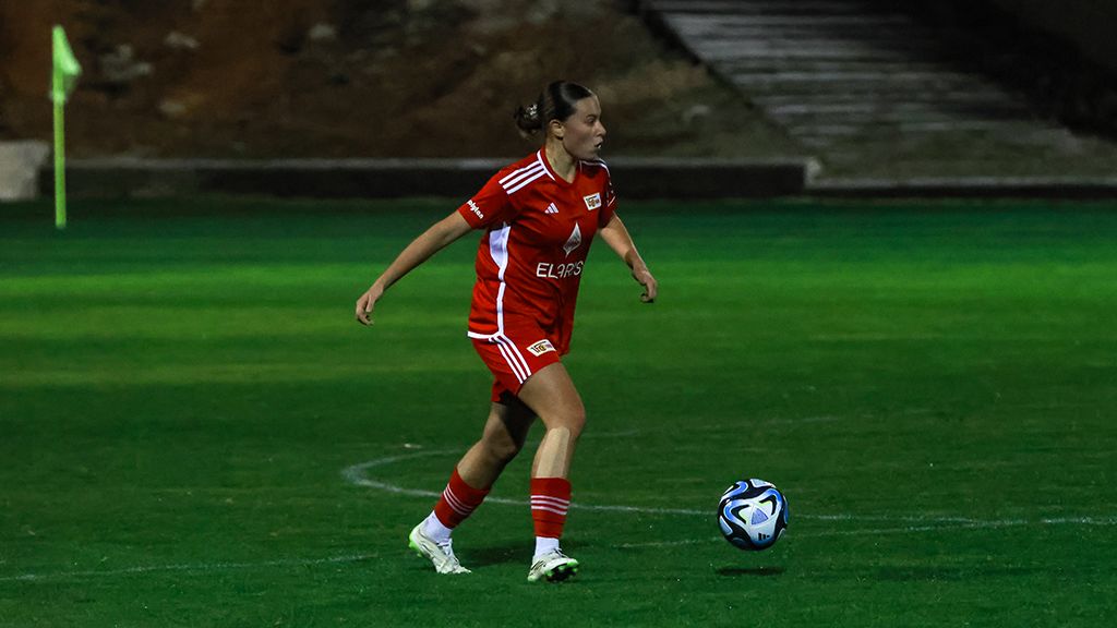 Spielerin in rotem Trikot läuft auf einem Fußballfeld und bereitet sich darauf vor, den Ball zu spielen.