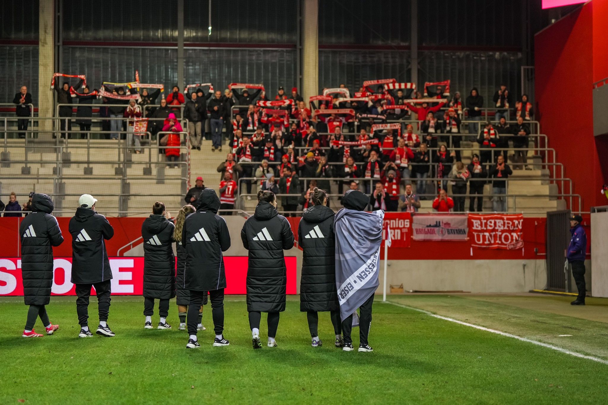 Fußballmannschaft feiert vor jubelnden Fans, die Schals halten, in einem Stadion.