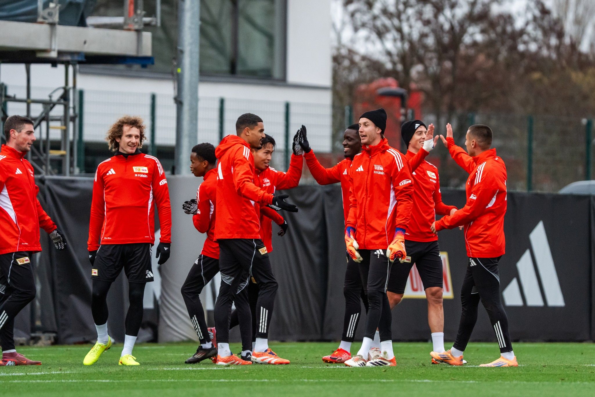 Die Spieler eines Fußballteams in roten Trikots stehen auf dem Trainingsplatz und haben Spaß miteinander.