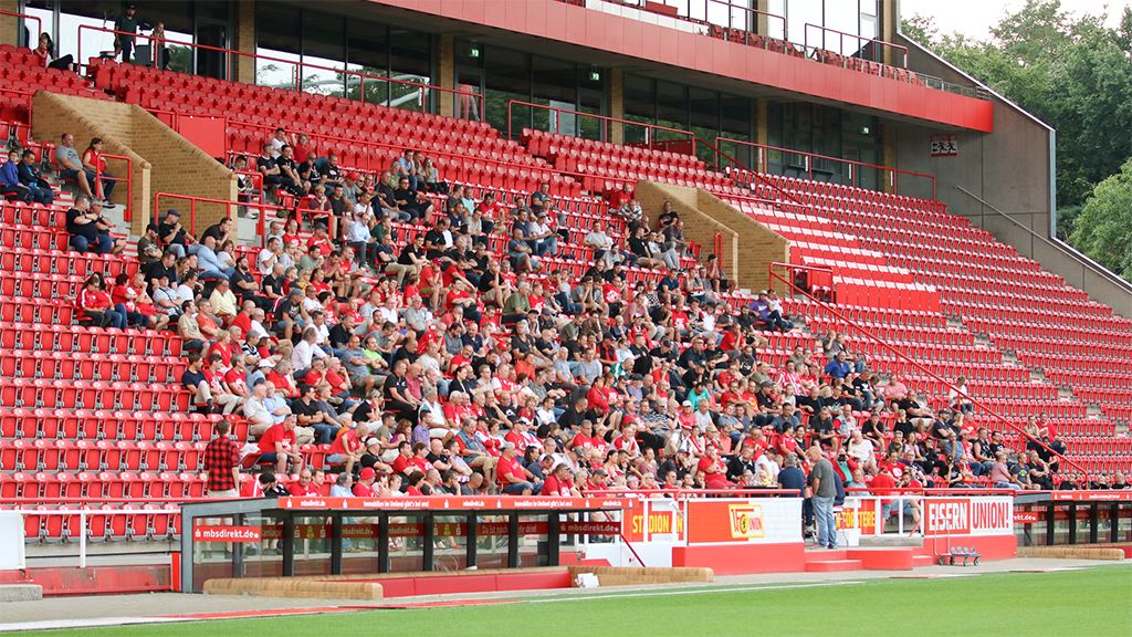 Vollbesetzte Tribüne in einem Fußballstadion mit roten Sitzen und Zuschauer in roten und neutralen Kleidungsstücken.