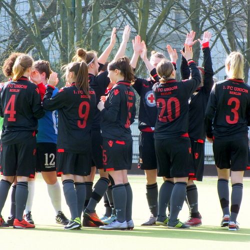 Eine Gruppe von weiblichen Fußballspielerinnen in schwarzen Trikots feiert und ist dabei, sich gegenseitig abzuklatschen.