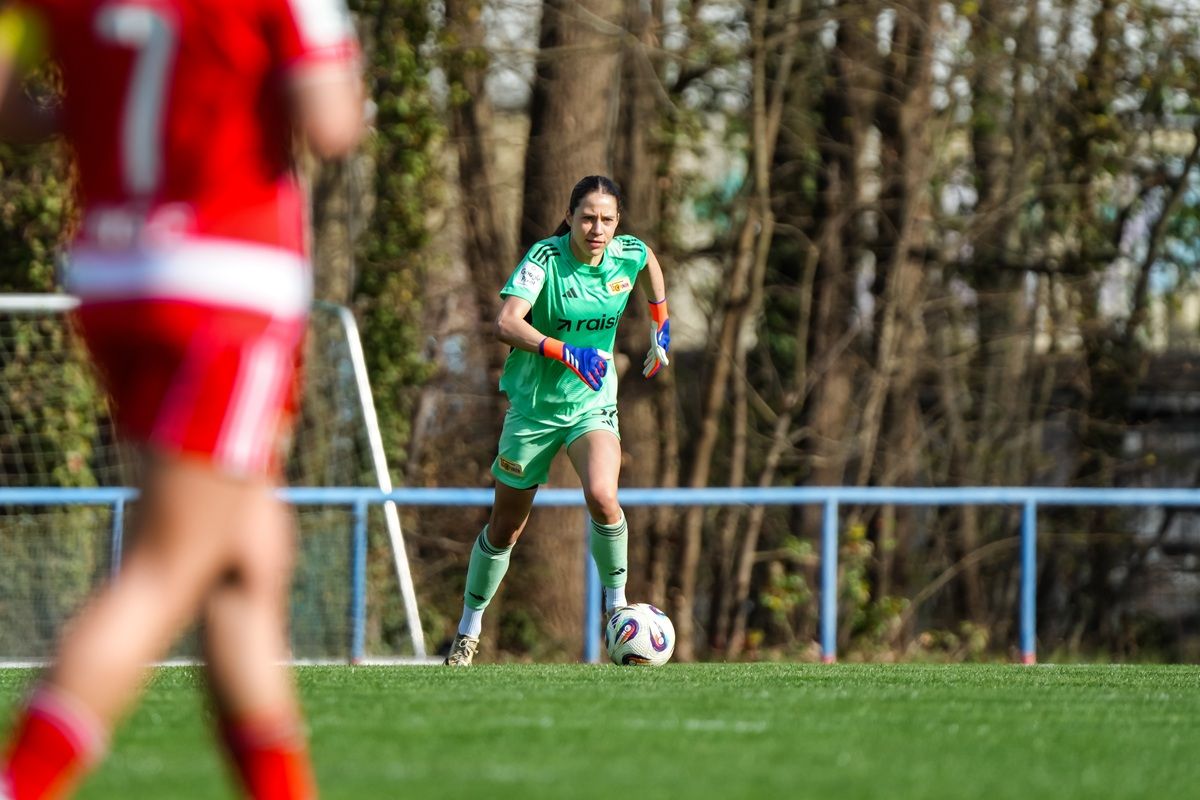 Eine Torhüterin in grüner Ausrüstung rennt über das Spielfeld, während eine gegnerische Spielerin im Hintergrund zu sehen ist.