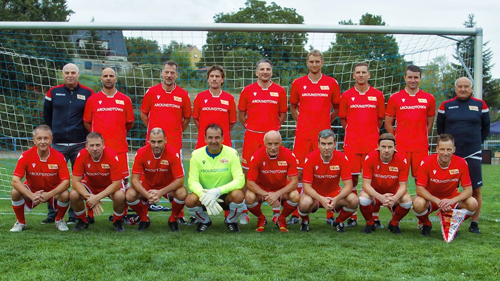 Eine Fußballmannschaft in roten Trikots steht in zwei Reihen vor einem Tor auf einem Rasenplatz.