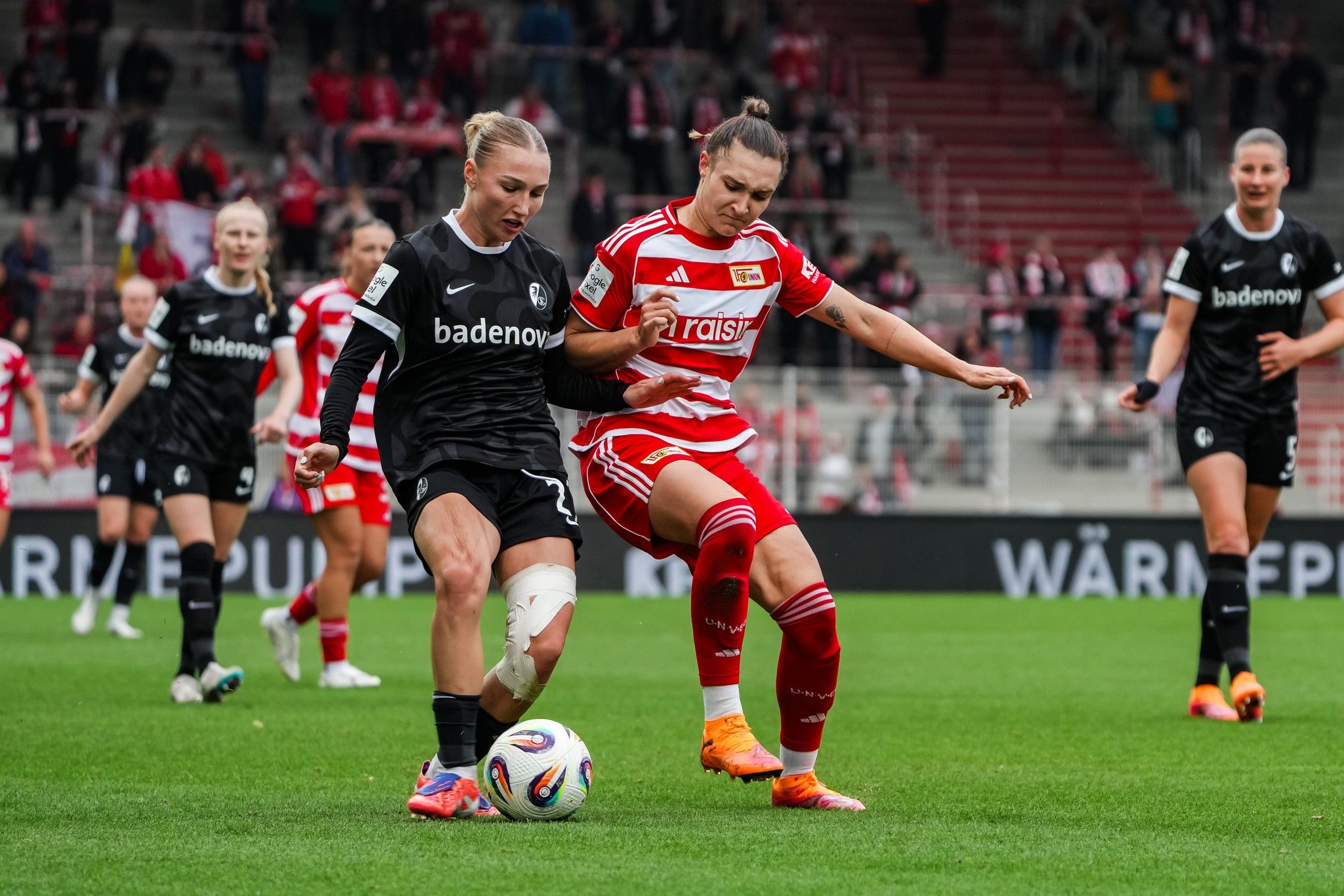 Zwei Fu ßballspielerinnen im Wettkampf um den Ball auf dem Spielfeld, umgeben von Zuschauern in einem Stadion.