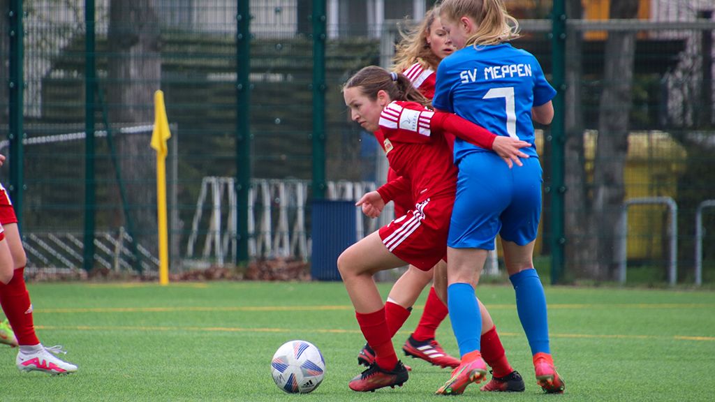 Zwei Mädchen in Fußballtrikots kämpfen um den Ball auf einem Kunstrasenplatz.
